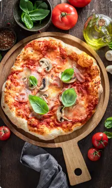 Vue de dessus d'une pizza garnie de basilic frais, champignons, et sauce tomate, servie sur une planche en bois. Autour, des ingrédients comme des tomates, du basilic, et une bouteille d'huile d'olive complètent la présentation.